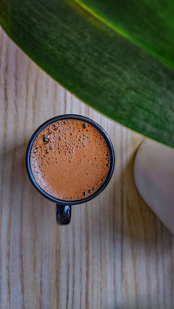 services-03 Top view of a coffee cup on wooden surface with a green leaf shadow.